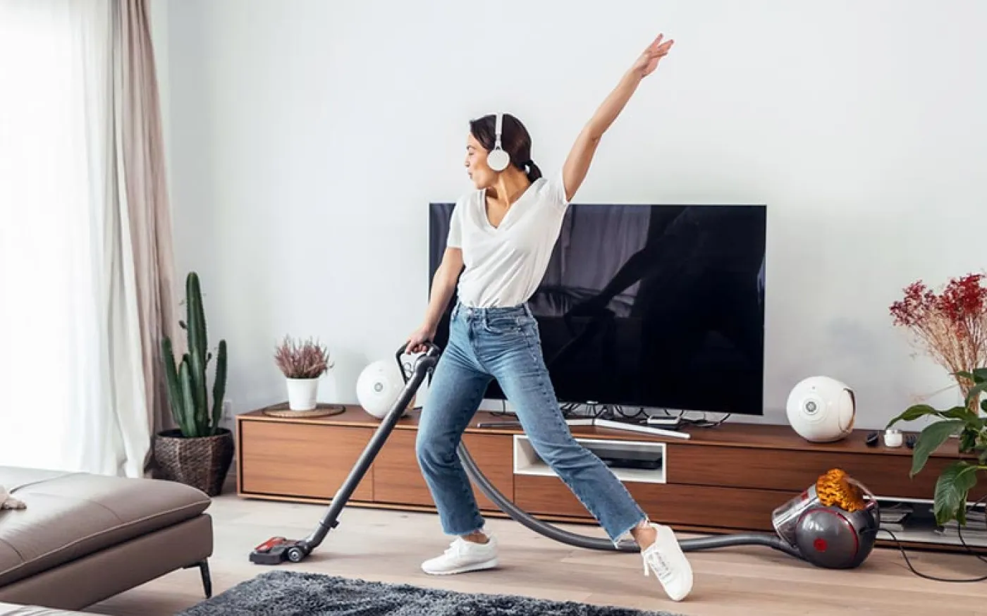 A young woman vacuuming her apartment with headphones on and dancing.